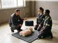 An instructor and two learners kneeling beside a first aid training manikin